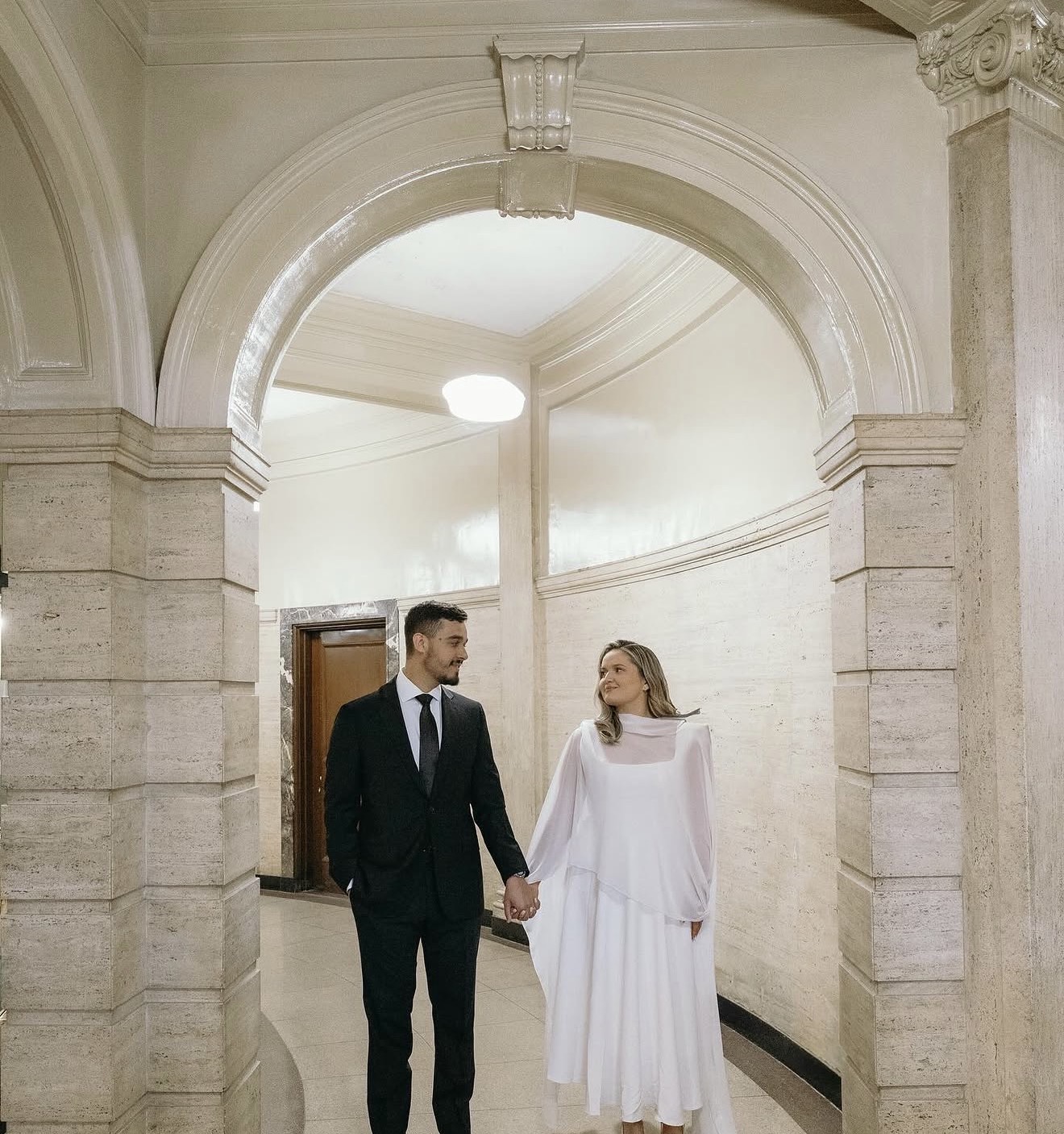 Matheus and Layza walking hand in hand beneath a stone archway
