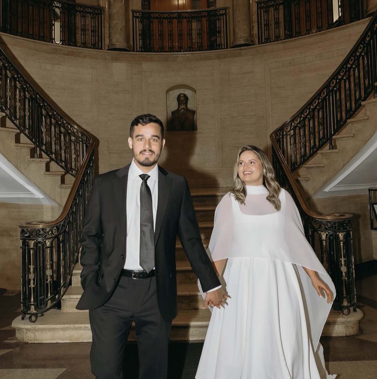 The couple hand in hand before the grand marble staircase